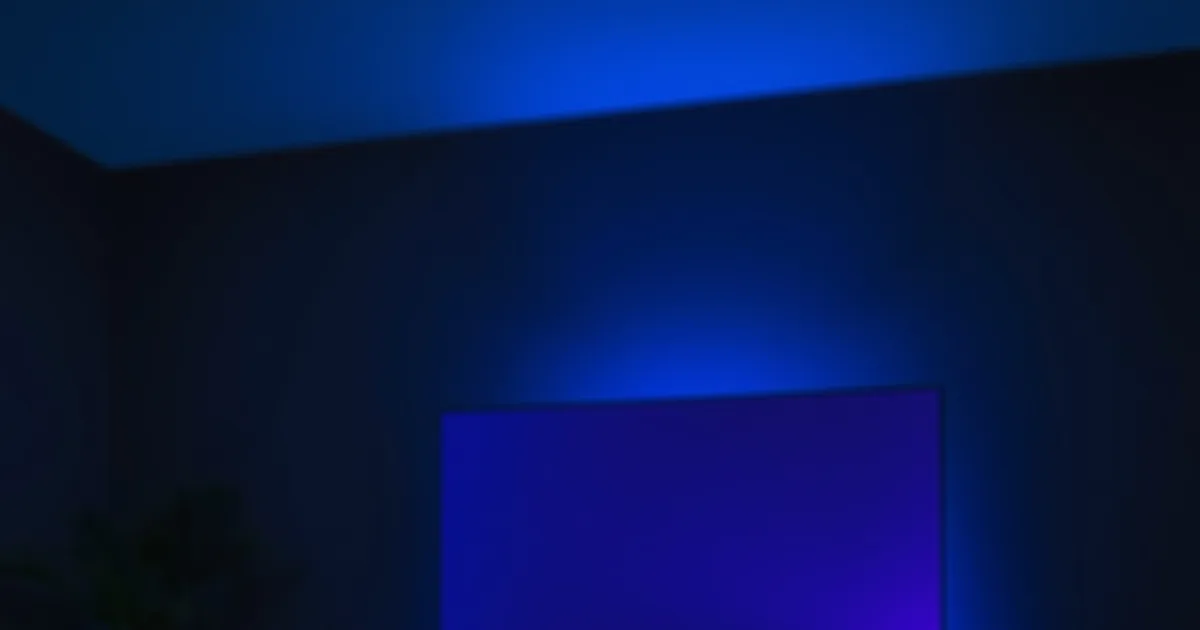 Dunkles Wohnzimmer bei Nacht, beleuchtet vom kalten blauen Schein eines laufenden IPTV-Streams auf dem Fernseher, Fernbedienung und Smartphone im Vordergrund